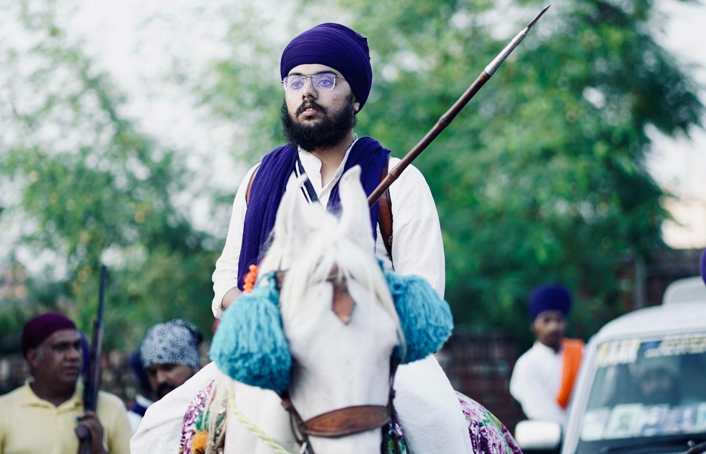 Groom on a decorated horse during a baraat procession with family dancing alongside
